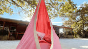 A child rests comfortably inside a pink Outree Sensory Pod Swing hanging from a tree on a sunny day.