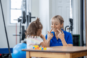 Speech therapist pointing to her mouth while modeling speech sounds for a toddler.